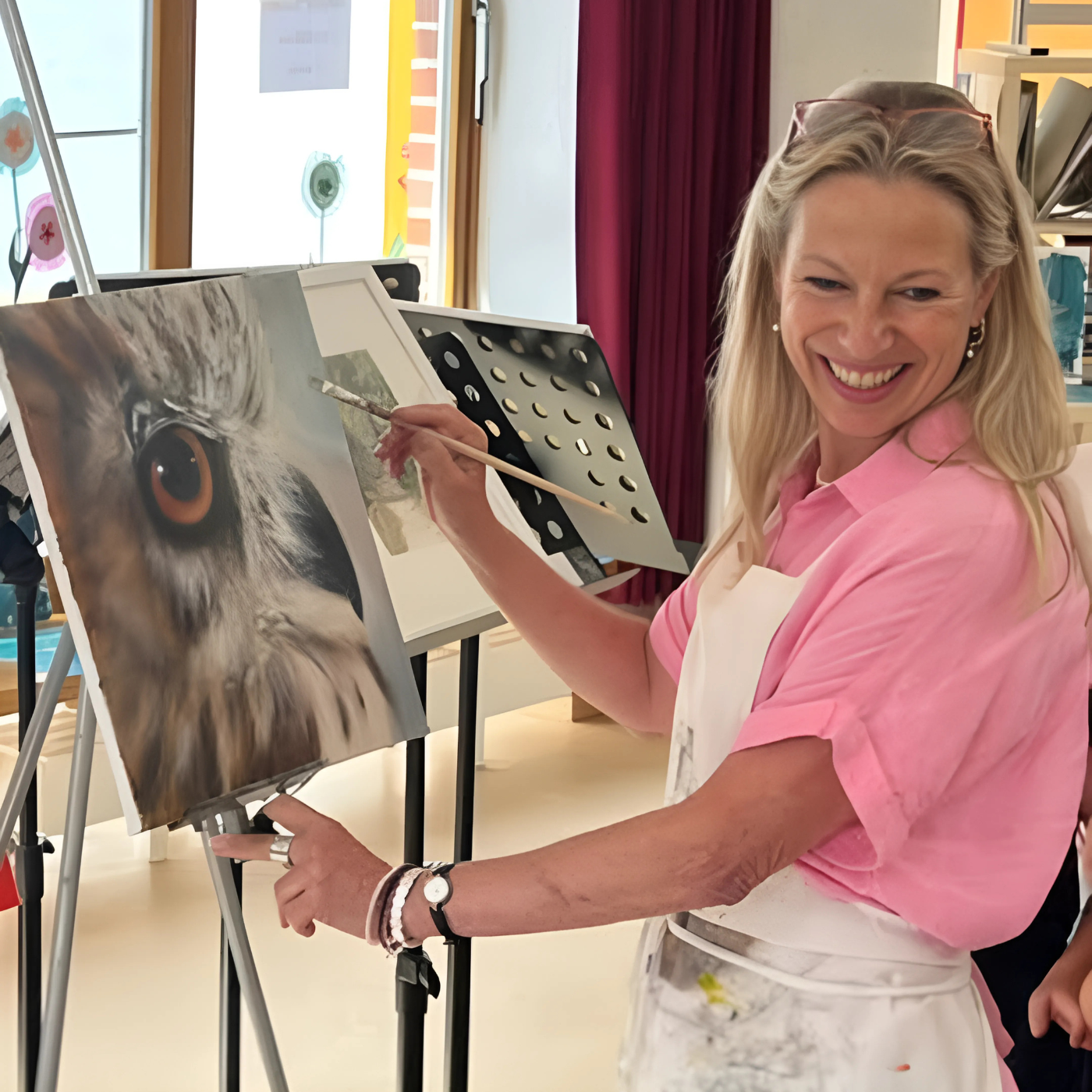 Anke Dinkelbach, Künstlerin von FemArtSPACE, vor einer grünen Leinwand mit Pinsel in der Hand. Ihr konzentrierter Ausdruck und die Farbtupfer auf der Leinwand verraten ihre künstlerische Leidenschaft. Im Hintergrund sind weitere Gemälde mit Pferdeköpfen zu erkennen, die einen Einblick in ihr künstlerisches Schaffen geben.