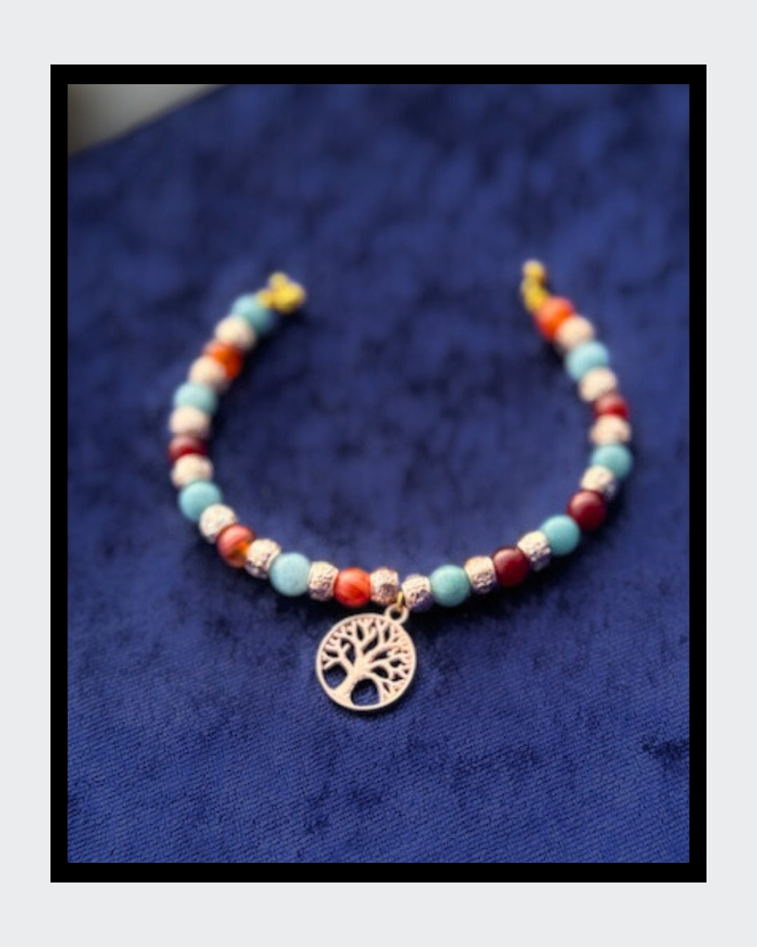 Edles Armband mit Aquamarin-Edelsteinen und roten Karneol-Zwischenteilen, ergänzt durch goldfarbene Rondelle. Im Mittelpunkt steht ein goldener Lebensbaum-Anhänger. Gefädelt auf goldfarbenem Draht und mit praktischem Magnetverschluss.