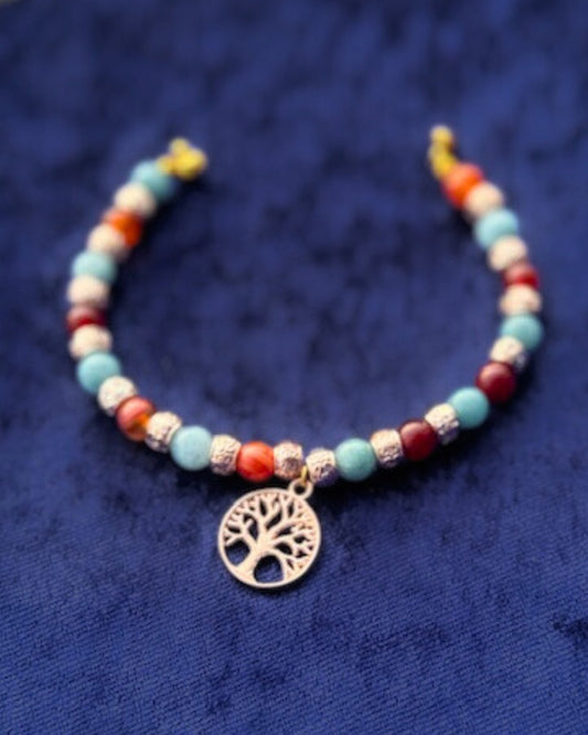 Edles Armband mit Aquamarin-Edelsteinen und roten Karneol-Zwischenteilen, ergänzt durch goldfarbene Rondelle. Im Mittelpunkt steht ein goldener Lebensbaum-Anhänger. Gefädelt auf goldfarbenem Draht und mit praktischem Magnetverschluss.