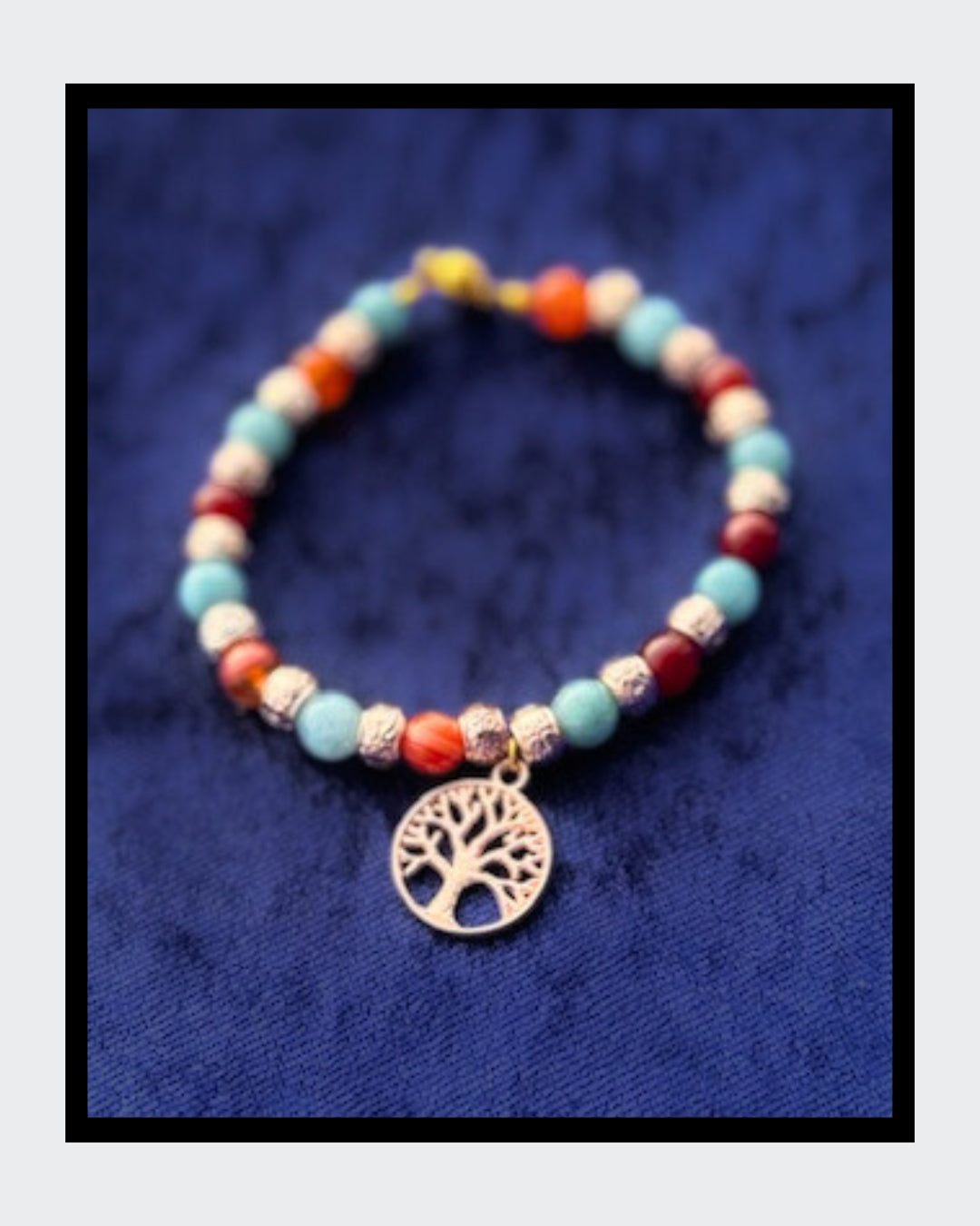 Edles Armband mit Aquamarin-Edelsteinen und roten Karneol-Zwischenteilen, ergänzt durch goldfarbene Rondelle. Im Mittelpunkt steht ein goldener Lebensbaum-Anhänger. Gefädelt auf goldfarbenem Draht und mit praktischem Magnetverschluss.