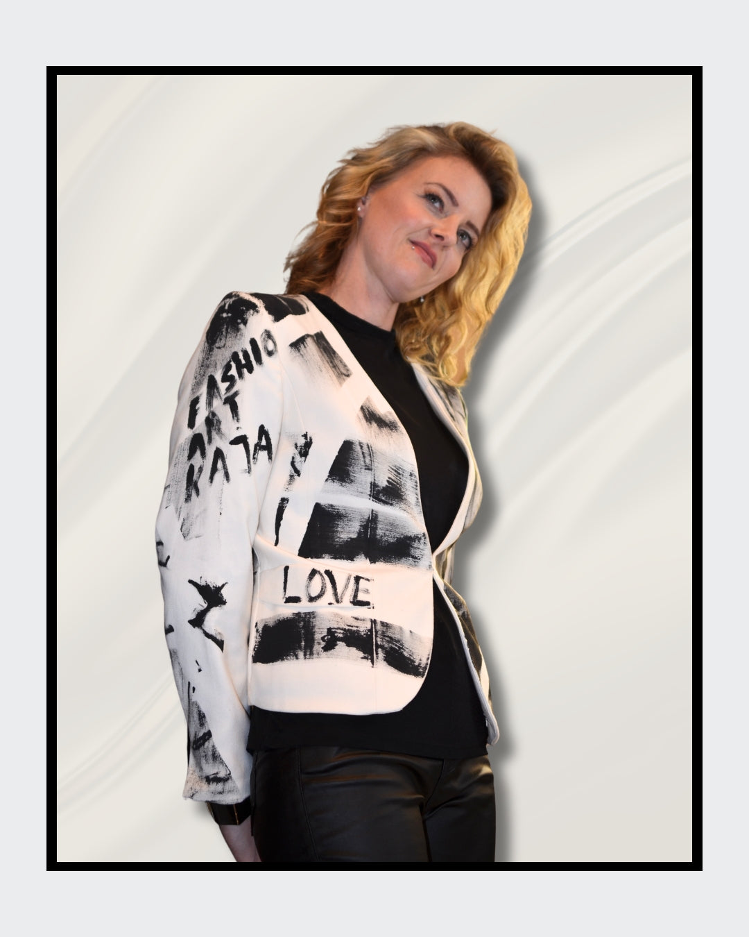 Eine blonde Frau steht vor einem cremefarbenen Hintergrund und blickt nach rechts. Sie trägt einen weißen Blazer mit schwarzen, abstrakten Mustern und Schriftzügen, darunter das Wort "LOVE". Darunter trägt sie ein schwarzes Oberteil und eine schwarze Hose. Fashionart von Kaja Schäfer, exklusiv bei FEMARTSPACE, Online-Galerie.