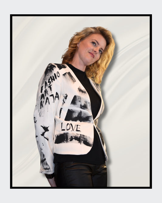 Eine blonde Frau steht vor einem cremefarbenen Hintergrund und blickt nach rechts. Sie trägt einen weißen Blazer mit schwarzen, abstrakten Mustern und Schriftzügen, darunter das Wort "LOVE". Darunter trägt sie ein schwarzes Oberteil und eine schwarze Hose. Fashionart von Kaja Schäfer, exklusiv bei FEMARTSPACE, Online-Galerie.