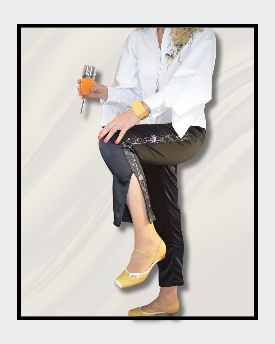Fashionart von Kaja Schäfer für FemArtSPACE: Die untere Hälfte einer Frau in einer eleganten Pose. Schwarze Satinhose mit silbernen und grauen Linien, gelbe Ballerinas und ein orangefarbenes Getränk in der Hand. Cremiger Hintergrund mit fließenden Stoffen.