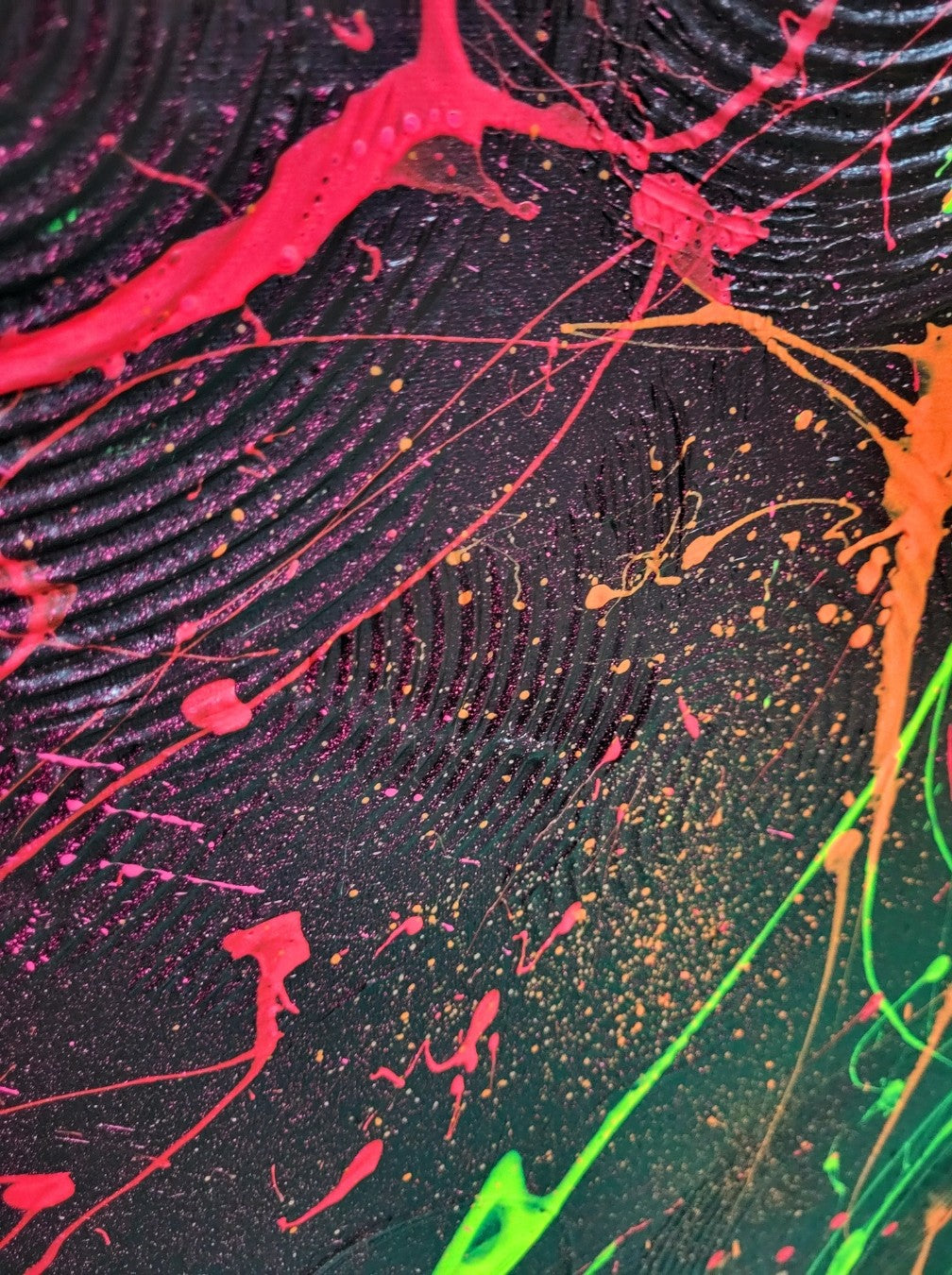 Abstraktes Acrylgemälde "Neon Galaxy" von Sandra Conrad, dominiert von einer dunklen Oberfläche, über die sich dynamische Spritzer und fließende Formen in fluoriszierendem Neon-Grün, Rot und Orange ziehen.
