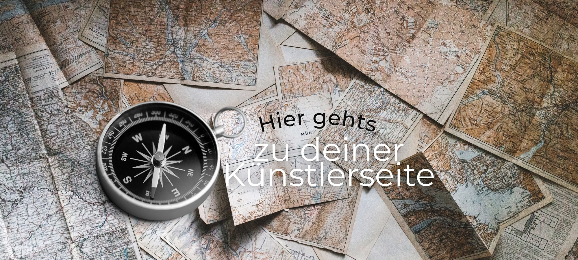 Mehrere aufgefaltete Vintage-Landkarten liegen überlappend ausgebreitet, darauf eine silberne Kompassnadel im Vordergrund. Rechts darüber steht in moderner, klarer Schrift: ‚Hier gehts zu deiner Künstlerseite‘