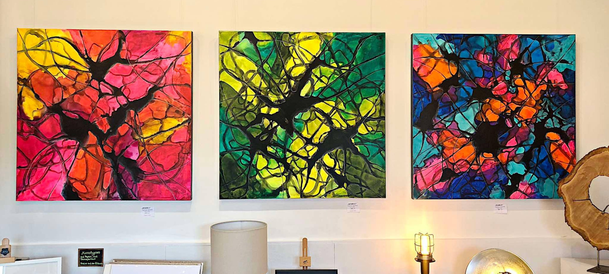 Abstrakte Kunst von Sabine Hoch-Himmighofen. Eine Triptychon-Installation aus drei farbintensiven Acrylbildern. Die lebendigen, transparenten Farbflächen in Pink, Gelb, Grün, Blau und Orange werden von dunklen, netzartigen Mustern überlagert, die eine dynamische Textur erzeugen.