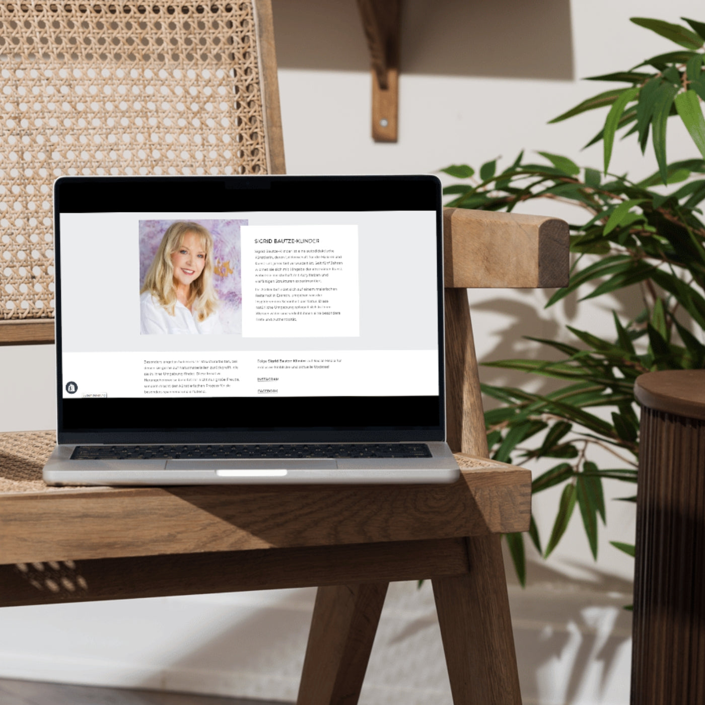 Laptop auf einem Holzstuhl zeigt die FemArtSPACE-Online-Galerie mit einer Künstlerin vor abstrakter Pastellkunst in Rosa- und Weißtönen, beleuchtet von natürlichem Licht.