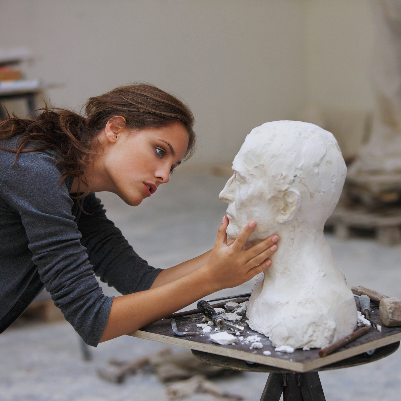 Bild einer Künstlerin im FemArtSPACE Artshop, die eine Büste aus Ton, mit Fokus auf die Detailarbeit in einem hellen Studio formt.